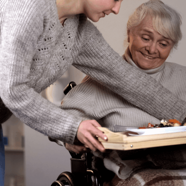 Imagen en la que una mujer lleva la comida a una señora en silla de ruedas.